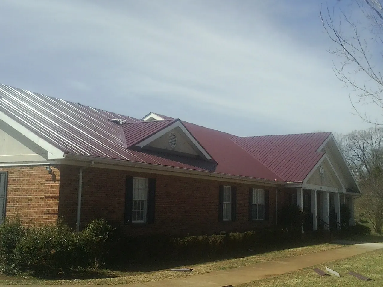 Red metal roof with gabled entries on a long brick building, from a Hail Damage Roof Repair job in Healdsburg