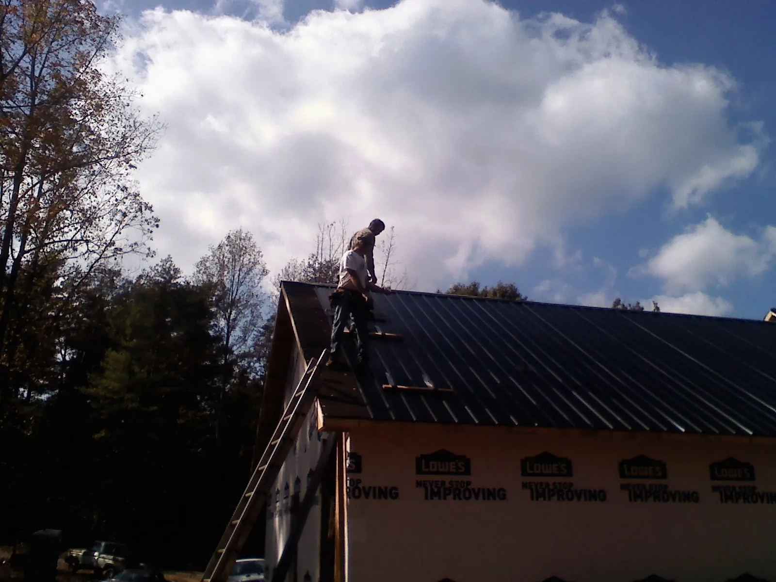 Roofer fastening dark metal panels high against a cloudy sky, from a Roof Inspection job in Healdsburg