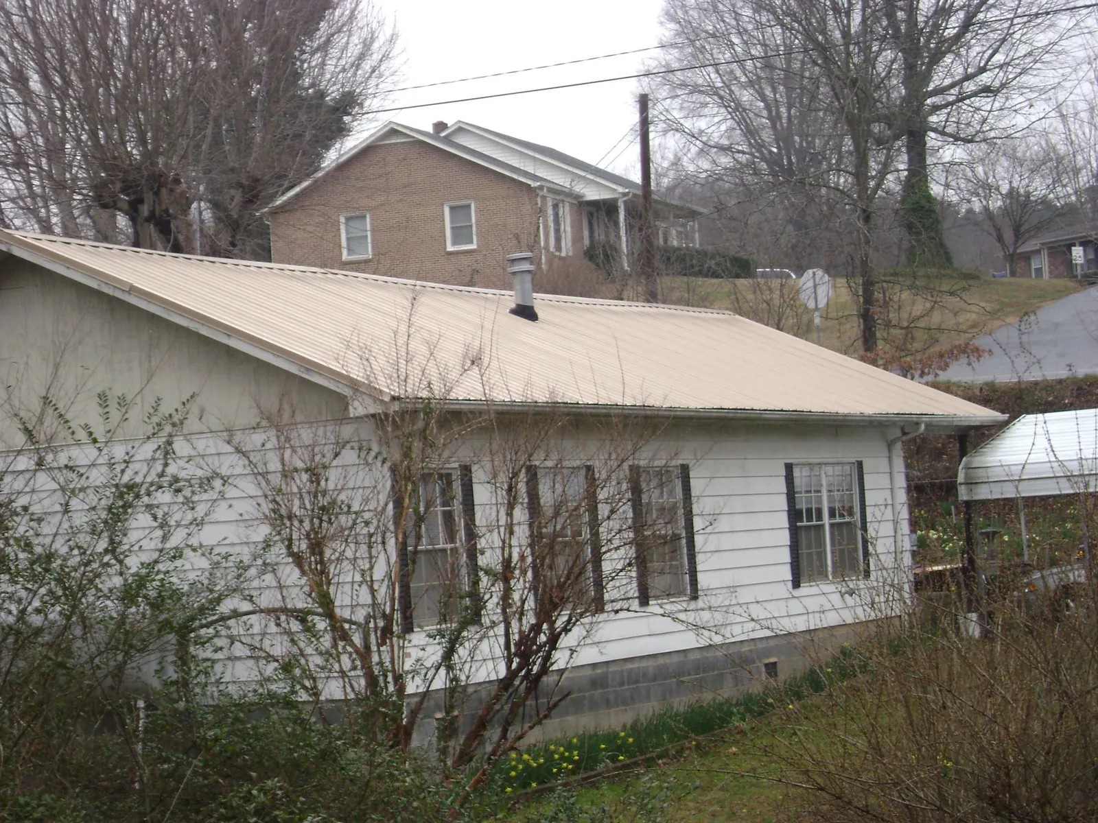 Tan metal roof on a white sided house set into a hillside — Commercial Roofing by Roofing Brothers in Healdsburg